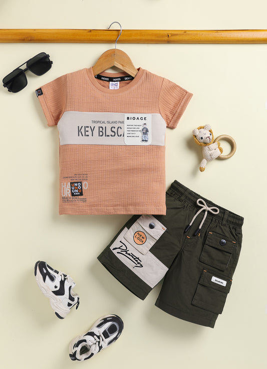 Image file 10407-Rust_2.jpg showing a flat lay of a Unokids brand boys two-piece clothing set featuring a textured rust-colored short-sleeve t-shirt with urban typographic graphics and dark olive green cargo shorts with an elastic drawstring waist and multiple functional pockets.