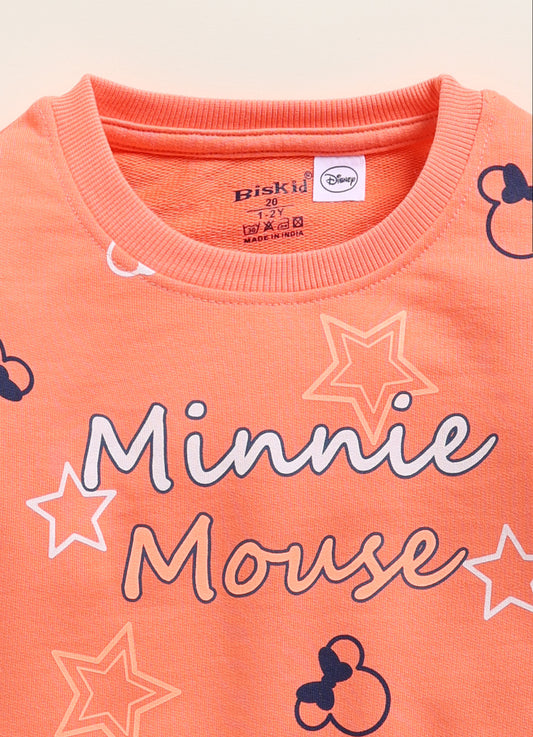 Image file 1751-Orange.jpg showing a Biskid brand girls orange fleece sweatshirt featuring an all-over Minnie Mouse silhouette and star print, displayed on a wooden hanger with children's sneakers and a decorative star accent nearby.