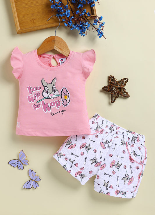 Flat lay of an Annie brand girls two-piece clothing set featuring a peach pink flutter-sleeve top with a too hip to hop Thumper rabbit graphic paired with white textured shorts featuring an all-over Thumper and pink flower print an elastic drawstring waist and pink pocket trim.
