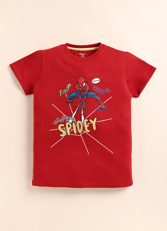 showing a smiling young boy with dark hair modeling a bright red Biskid brand short-sleeve t-shirt. The shirt features an action graphic of Spider-Man crouching and shooting webs, surrounded by the text "AMAZING SPIDEY" and comic-style sound effect words.