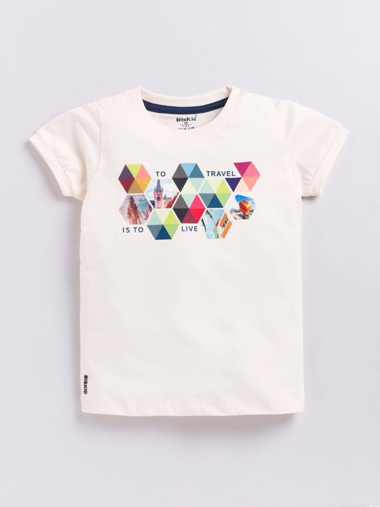 a young boy with curly hair modeling a Biskid brand cream-colored short-sleeve t-shirt. The shirt features a geometric graphic made of colorful pastel hexagons and triangles containing travel photos, accompanied by the text "TO TRAVEL IS TO LIVE".