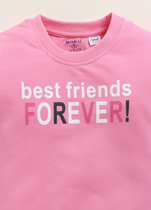 Image file 1754-Pink.jpg showing a Biskid brand girls pink fleece sweatshirt featuring the text "best friends FOREVER!" on the front, displayed on a wooden hanger with a small plush bunny toy and a heart-shaped woven decoration nearby.