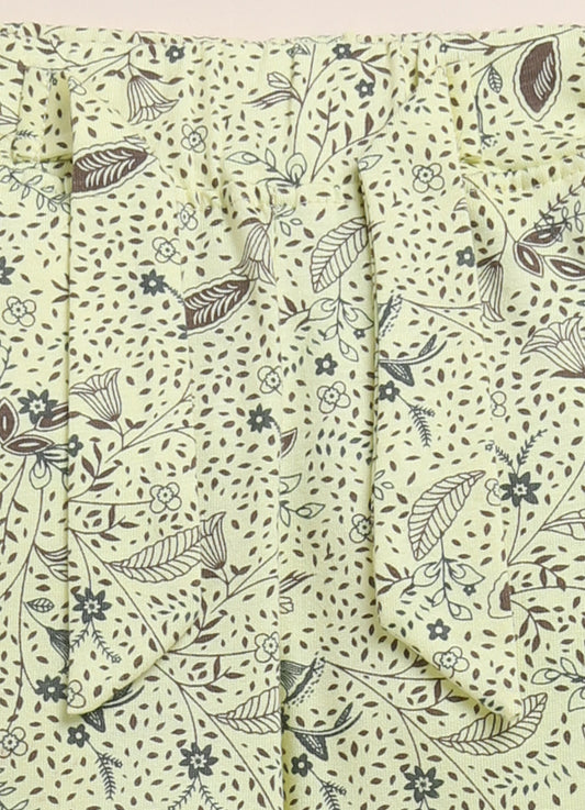 Image file 1512-Lemon.jpg showing a pair of Biskid brand girls' lemon yellow long pants with an all-over botanical print, displayed on a woven mat with pink sunglasses, a toy camera, and yellow decorative flowers nearby.