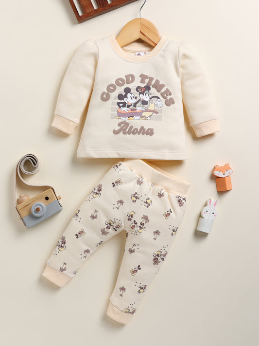 Image showing a flat lay of an Annie brand girls two-piece clothing set. The outfit includes a cream-colored long-sleeve top with a "GOOD TIMES Aloha" graphic featuring Mickey and Minnie Mouse, paired with matching cream-colored joggers covered in a whimsical all-over print of Mickey and Minnie with palm trees.