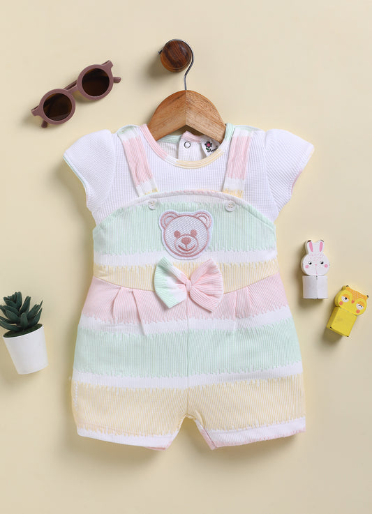 Annie brand girls short-sleeve jumpsuit designed to look like a textured white top underneath pastel green, yellow, and pink striped overall shorts. The outfit features an embroidered pink bear face on the chest, a decorative striped bow, and a back snap closure.