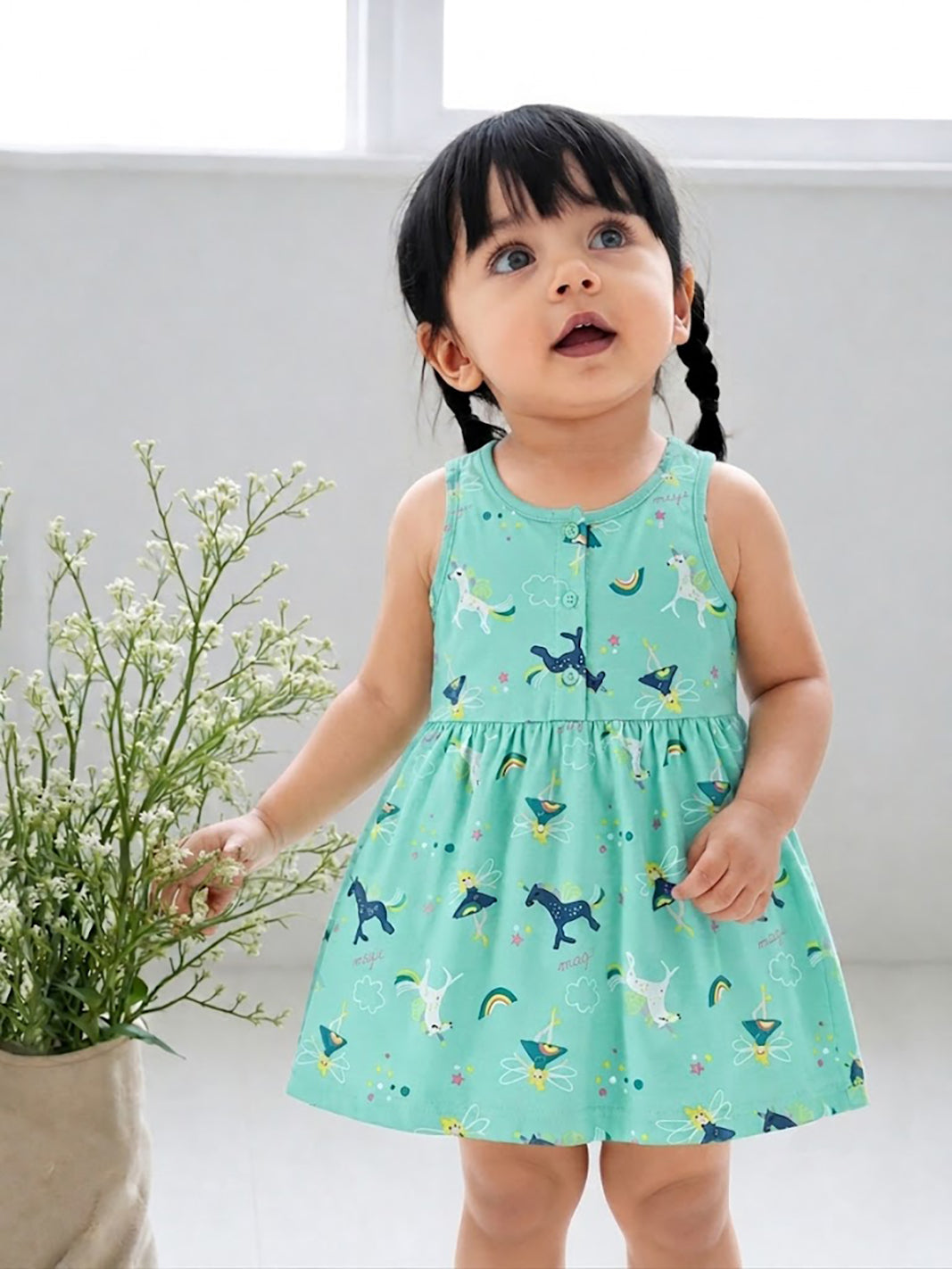 Flat lay of an Annie brand girls sleeveless pink frock featuring a gently gathered waist and an all-over magical print with white and blue unicorns, fairies, rainbows, clouds, and stars.