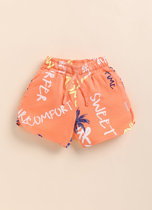 Image file 1409-Peach.jpg showing a pair of Biskid brand peach girls shorts with an elastic drawstring waistband, covered in an all-over beach-themed typography print featuring words like "SWEET" and "COMFORT," with a small "BISKID" brand tag on the side.