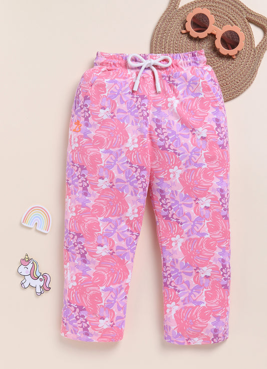 Image file 1511-Pink.jpg showing a pair of Biskid brand girls pink joggers with an all-over tropical leaf print, displayed with fun decorative accents like a rainbow, a unicorn sticker, and flower-shaped sunglasses.