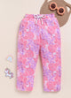 Image file 1511-Pink.jpg showing a pair of Biskid brand girls pink joggers with an all-over tropical leaf print, displayed with fun decorative accents like a rainbow, a unicorn sticker, and flower-shaped sunglasses.