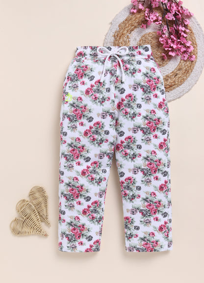 Image file 1511-Rust.jpg showing a pair of Biskid brand girls white joggers with an all-over floral rose print in rust and gray, displayed with a decorative woven mat, pink floral accents, and woven heart decorations.