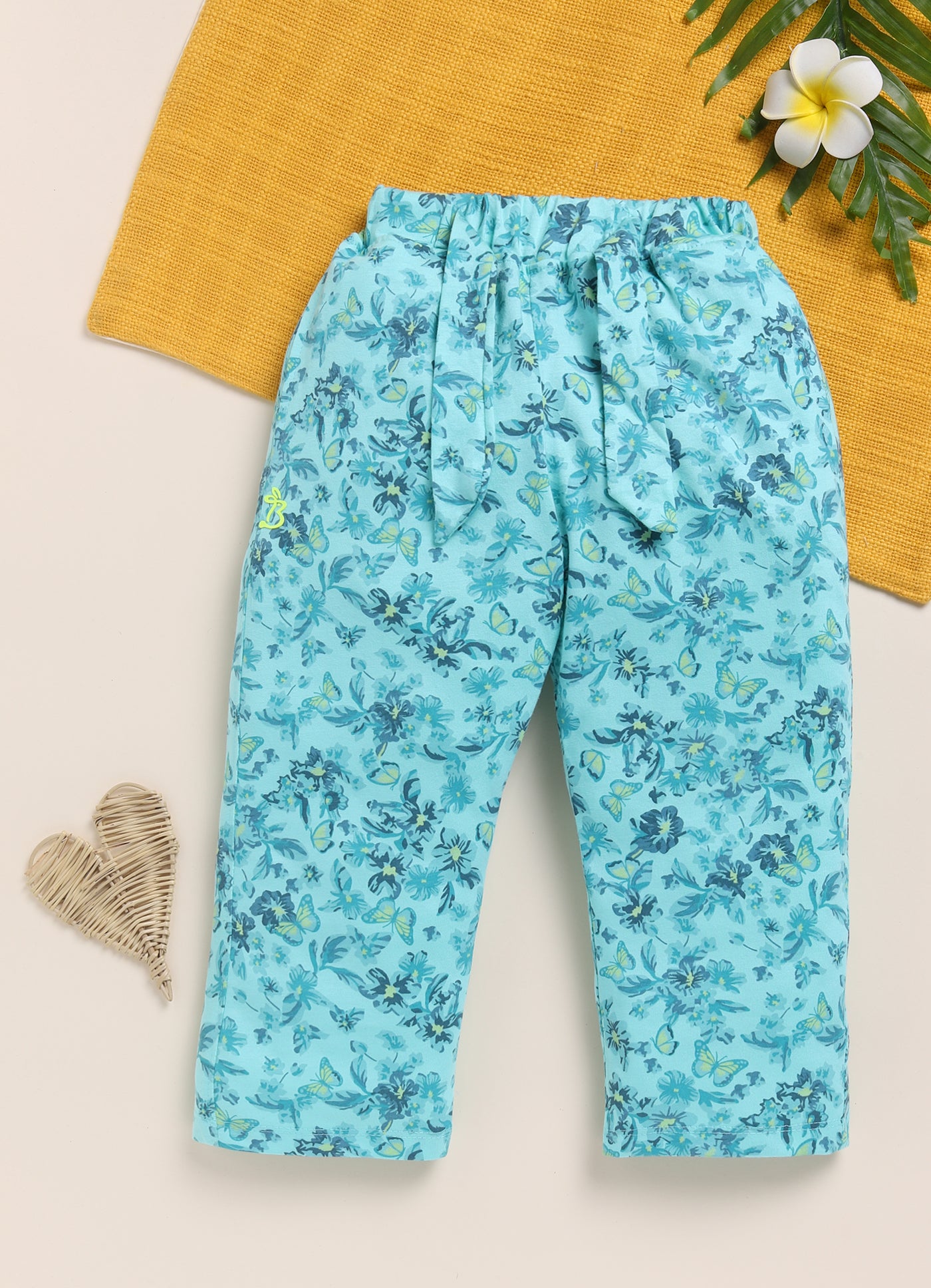 Image file 1512-P.Blue.jpg showing a pair of Biskid brand girls' powder blue long pants with an all-over floral and butterfly print, displayed with flower-shaped sunglasses, two decorative butterfly cutouts, and small blue floral accents nearby.