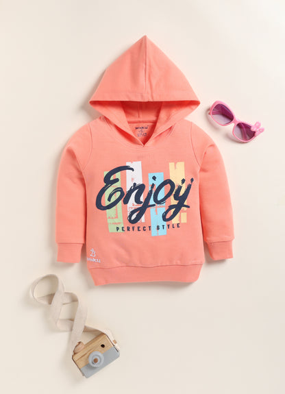 Image file 1756-Peach.jpg showing a flat lay of a peach Biskid brand girls hooded sweatshirt featuring the "Enjoy" graphic and "PERFECT STYLE" text, displayed with decorative items including children's sunglasses and a toy camera.