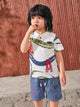 Flat lay of a TODOS brand boys two-piece clothing set featuring a white textured short-sleeve henley shirt with blue and green abstract waves and large red LA letters, paired with blue shorts with a black and white drawstring waist, Fashion embroidered in red on the right leg, and a TODOS logo patch on the left cargo pocket.