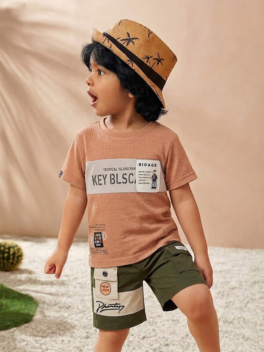 Image file 10407-Rust_2.jpg showing a flat lay of a Unokids brand boys two-piece clothing set featuring a textured rust-colored short-sleeve t-shirt with urban typographic graphics and dark olive green cargo shorts with an elastic drawstring waist and multiple functional pockets.