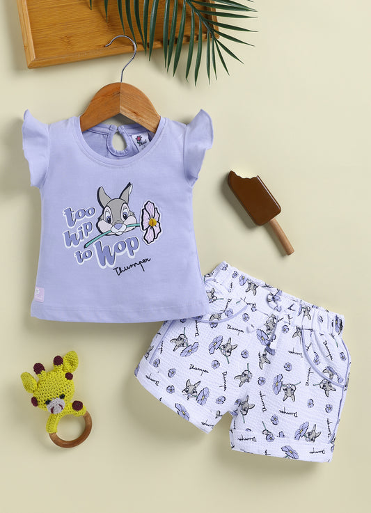 Flat lay of an Annie brand girls two-piece clothing set featuring a light purple flutter-sleeve top with a too hip to hop Thumper rabbit graphic paired with white textured shorts featuring an all-over Thumper and purple flower print an elastic drawstring waist and purple pocket trim.