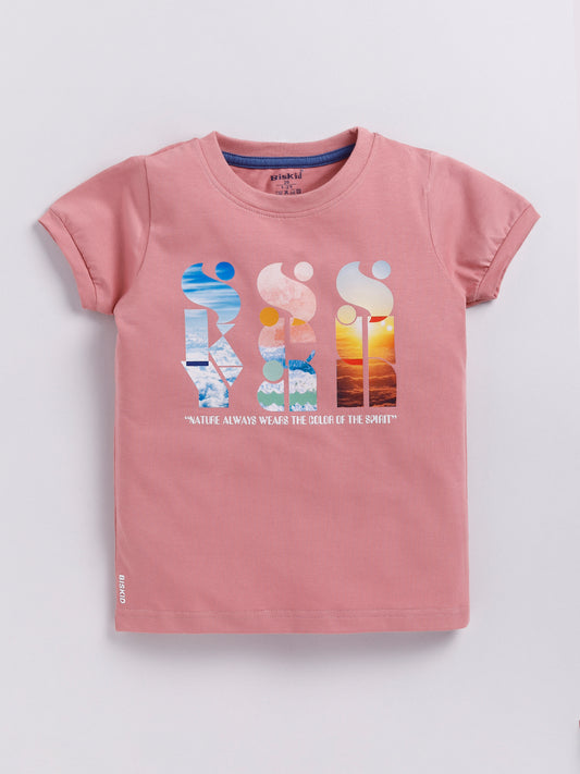 a young boy with curly hair modeling a dusty pink Biskid brand short-sleeve t-shirt. The shirt features an artistic chest graphic with the words "SKY", "SEA", and "SUN" written vertically and filled with nature photography, positioned above the quote "NATURE ALWAYS WEARS THE COLORS OF THE SPIRIT".