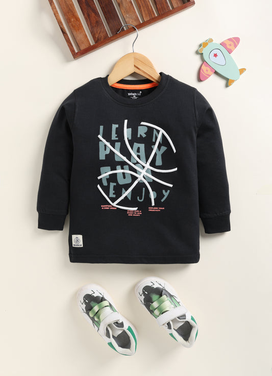 Image file Gemini_Generated_Image_fkez91fkez91fkez.jpg showing a young boy wearing a black Biskid brand boys long-sleeve t-shirt with a basketball-themed "Learn Play Fun Enjoy" graphic on the chest, paired with gray checkered shorts and white sneakers.