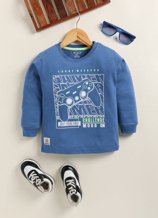 Image file Gemini_Generated_Image_u1773xu1773xu177.jpg showing a young boy wearing a blue Biskid brand boys long-sleeve t-shirt with a "Gamer" gaming controller graphic on the chest, paired with gray checkered shorts and white sneakers.