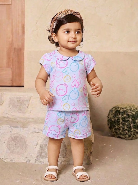 Annie brand girls two-piece clothing set featuring a sky blue short-sleeve top with a Peter Pan collar and matching shorts. Both pieces feature an all-over pastel print of doodle smiley faces, hearts, and the word HELLO in pink, blue, and yellow. The shorts have an elastic drawstring waist and front pockets.