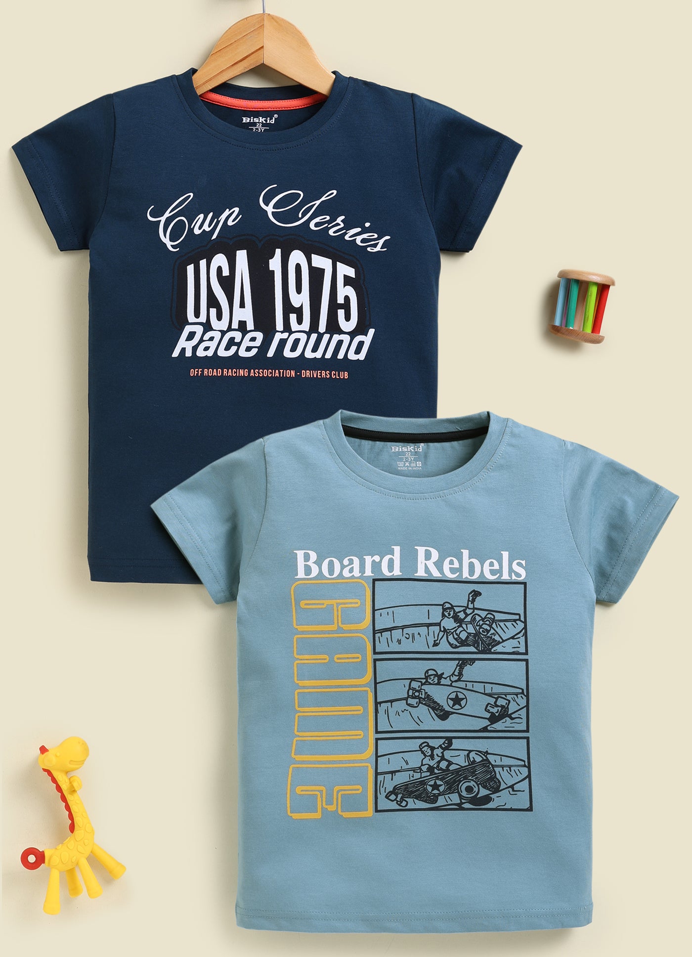 Image file 877-Blu--877-P.Blu.jpg showing a 2-pack of Biskid boys short-sleeve t-shirts featuring graphic prints, including a navy blue tee with "Cup Series USA 1975" typography and a pastel blue tee with "Board Rebels GAME" skateboard comic graphics.