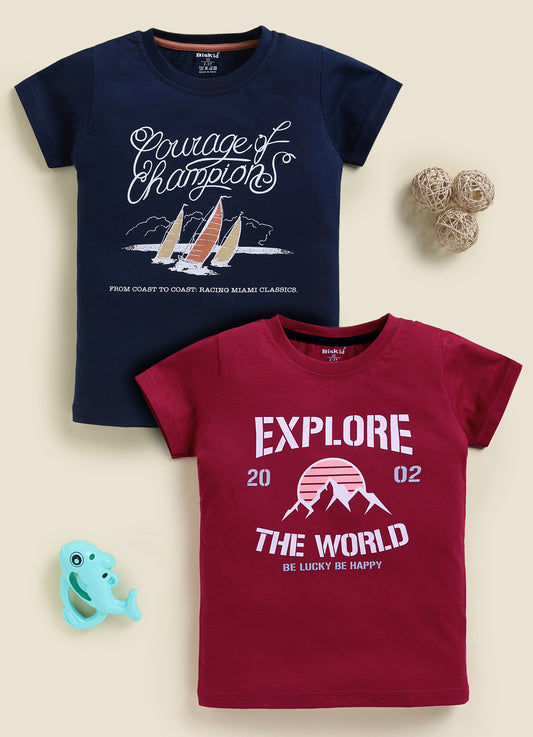 Image file 878-Nvy--878-Mron.jpg showing a 2-pack of Biskid boys short-sleeve t-shirts featuring graphic prints, including a navy blue tee with a "Courage of Champions" sailboat graphic and a maroon red tee with an "EXPLORE THE WORLD" mountain sunset print.