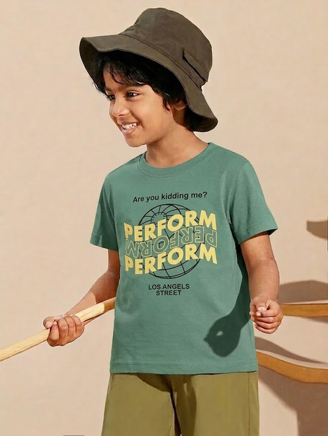 Image file 877-Green.jpg showing a Biskid brand boys' forest green crew neck t-shirt with a bold "PERFORM" graphic print on the front, displayed on a wooden hanger with small wooden spinning tops and colorful wooden "KIDS" letters nearby.