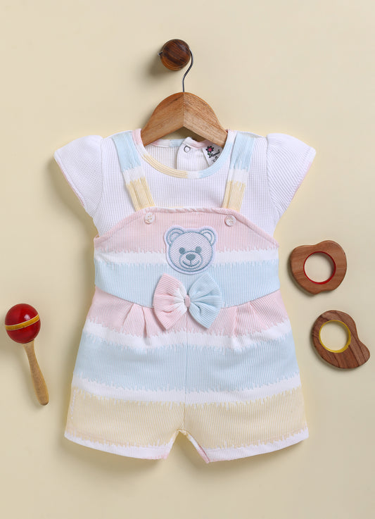  Annie brand girls short-sleeve jumpsuit designed to look like a textured white top underneath pastel pink, blue, and yellow striped overall shorts. The outfit features an embroidered bear face on the chest, a decorative bow, and a back snap closure.