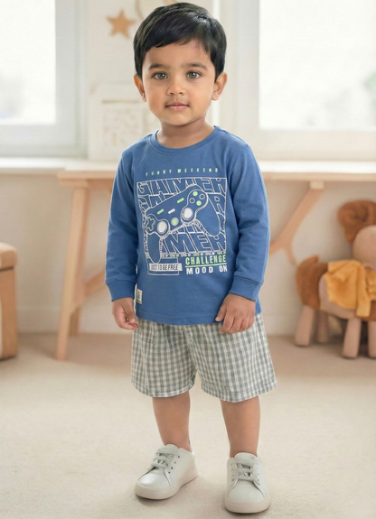 Image file Gemini_Generated_Image_u1773xu1773xu177.jpg showing a young boy wearing a blue Biskid brand boys long-sleeve t-shirt with a "Gamer" gaming controller graphic on the chest, paired with gray checkered shorts and white sneakers.