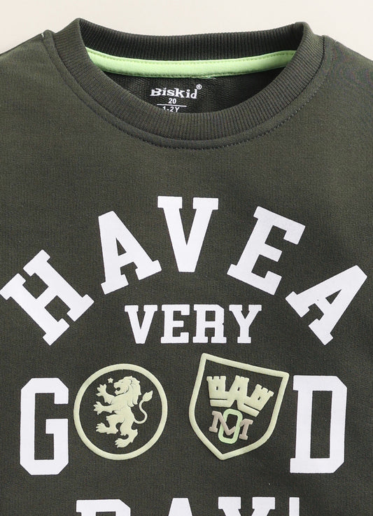 Image file Colour correction (3).jpg showing a flat lay of an olive green Biskid brand boys long-sleeve sweatshirt featuring "HAVE A VERY GOOD DAY!" text and emblem graphics, with a ribbed crew neck, cuffs, and hem.