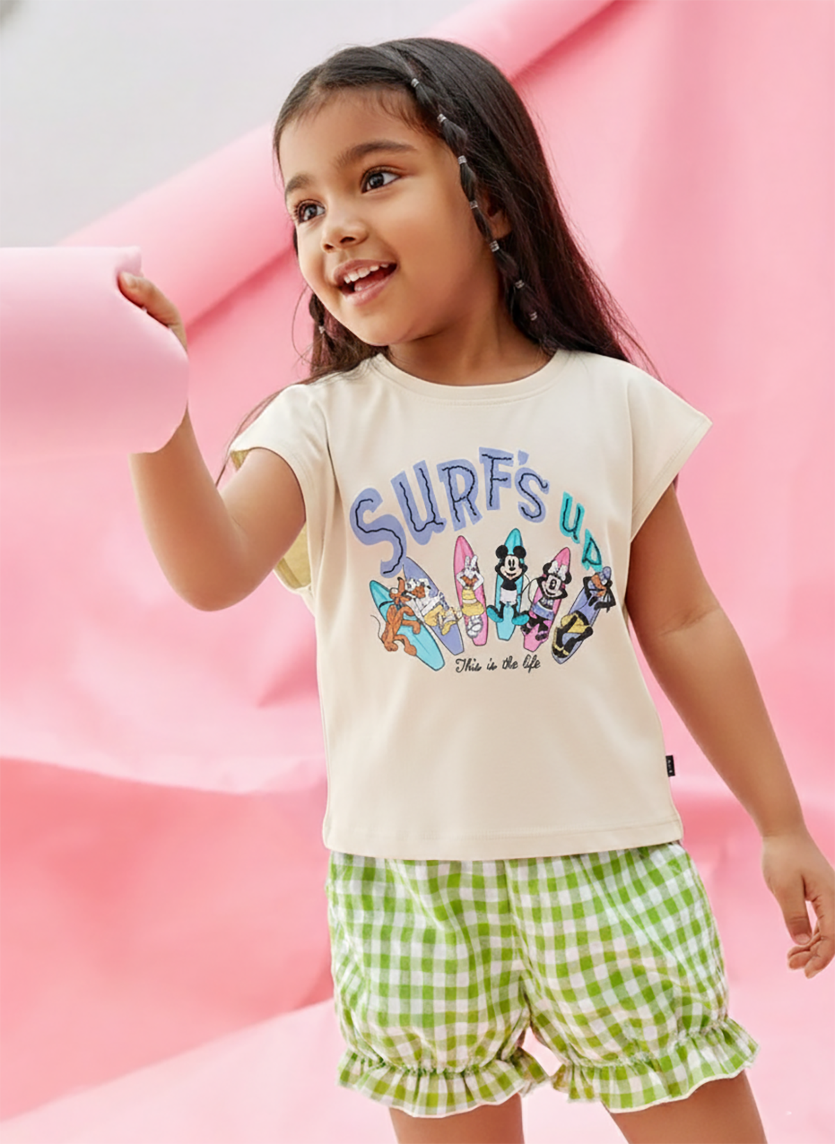 Image file showing a 2-pack of Biskid girls short-sleeve tops featuring Disney prints, including a cream top with a "Surfs Up" character surfboards graphic and a mint green top with Minnie Mouse and Daisy Duck graphics.