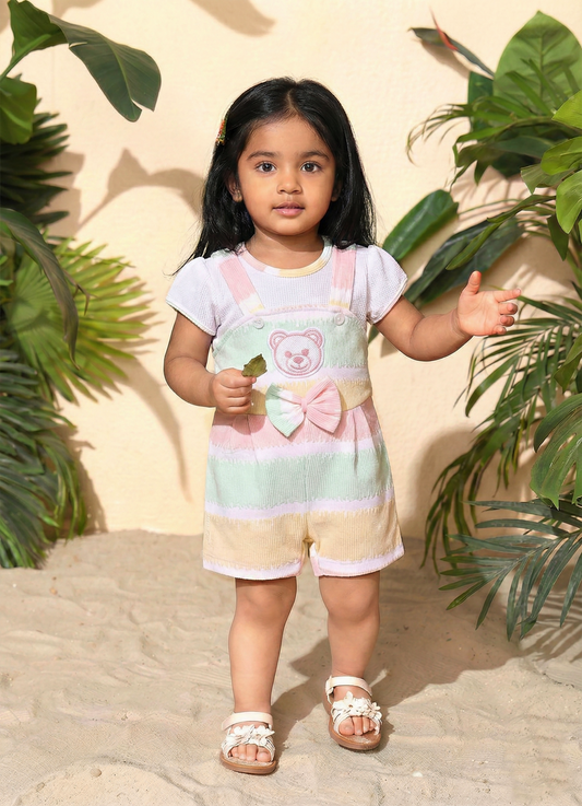 Annie brand girls short-sleeve jumpsuit designed to look like a textured white top underneath pastel green, yellow, and pink striped overall shorts. The outfit features an embroidered pink bear face on the chest, a decorative striped bow, and a back snap closure.