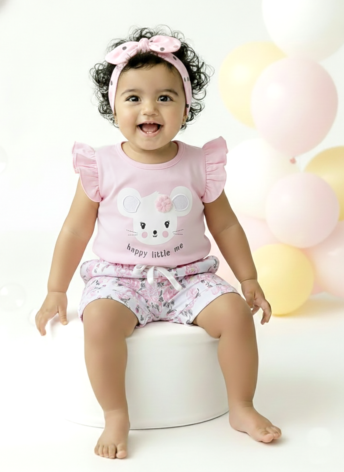Annie brand girls two-piece clothing set featuring a soft peach flutter-sleeve top with a mouse graphic, 3D flower applique, and the text "happy little me", paired with white shorts featuring a beautiful peach floral print, cuffed hems, and a ruffled elastic waist.