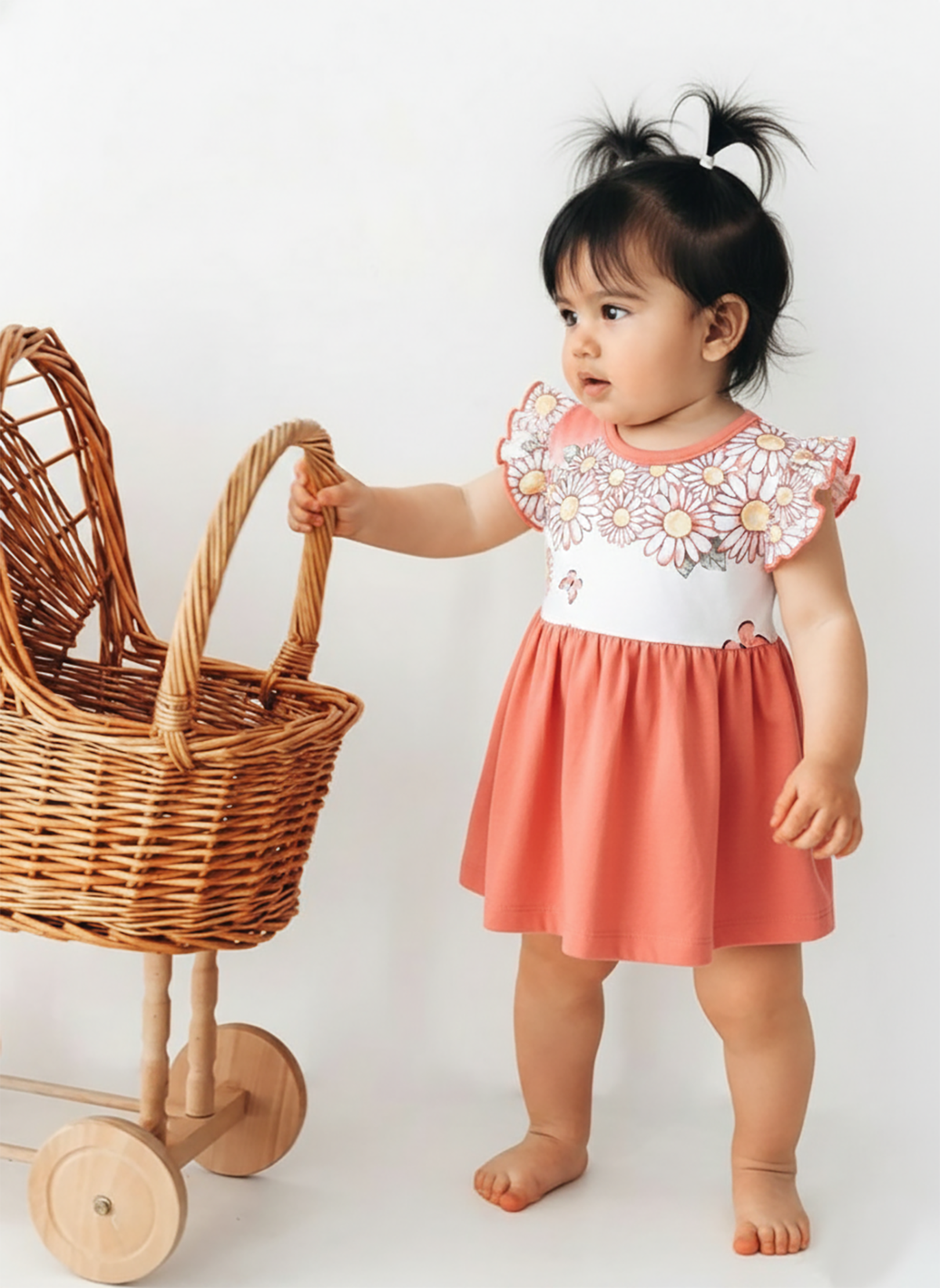 Annie brand girls two-piece frock and panty set. The dress features a white flutter-sleeve bodice with a coral red daisy and butterfly print, a back snap closure, and a solid coral red gathered skirt. It comes with a matching white bloomer panty featuring coral red ruffled trim on the leg openings.