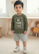 Image file Gemini_Generated_Image_ijt6gaijt6gaijt6.jpg showing a young boy wearing an olive green Biskid brand boys long-sleeve t-shirt with a "Be Your Self" graphic on the chest, paired with gray checkered shorts and white sneakers.