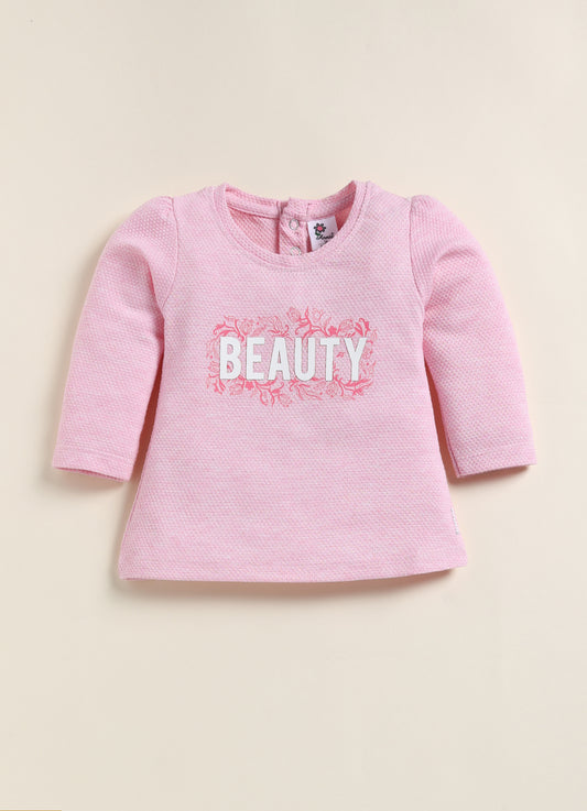 showing a flat lay of an Annie brand girls two-piece clothing set. The outfit includes a textured pink long-sleeve top with the word "BEAUTY" and floral accents, paired with matching leggings featuring a pink and white checkerboard pattern decorated with simple flowers.
