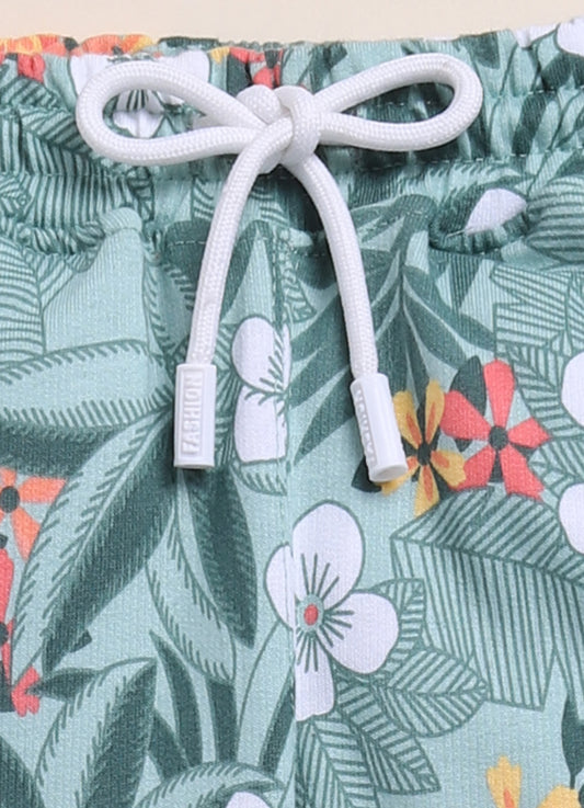 Image file 1511-M.Green.jpg showing a pair of Biskid brand girls mint green joggers with an all-over tropical floral print, featuring an elastic waistband with a white drawstring, displayed with decorative sunglasses, flowers, and greenery.