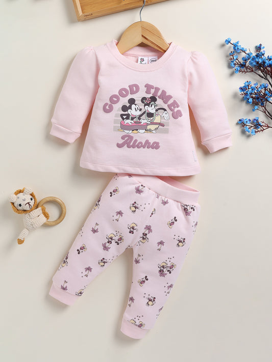 Image showing a flat lay of an Annie brand girls two-piece clothing set. The outfit includes a light pink long-sleeve top with a "GOOD TIMES Aloha" graphic featuring Mickey and Minnie Mouse, paired with matching light pink joggers covered in a whimsical all-over print of Mickey and Minnie with palm trees.