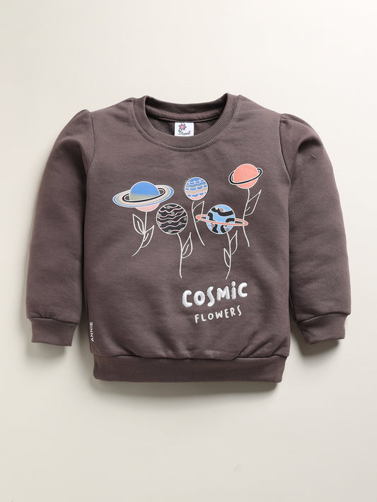 Image showing a flat lay of an Annie brand girls two-piece clothing set. The outfit includes a sage long-sleeve sweatshirt with a "COSMIC FLOWERS" graphic featuring stylized planets, paired with grey joggers covered in an all-over whimsical print of various planets and stars.