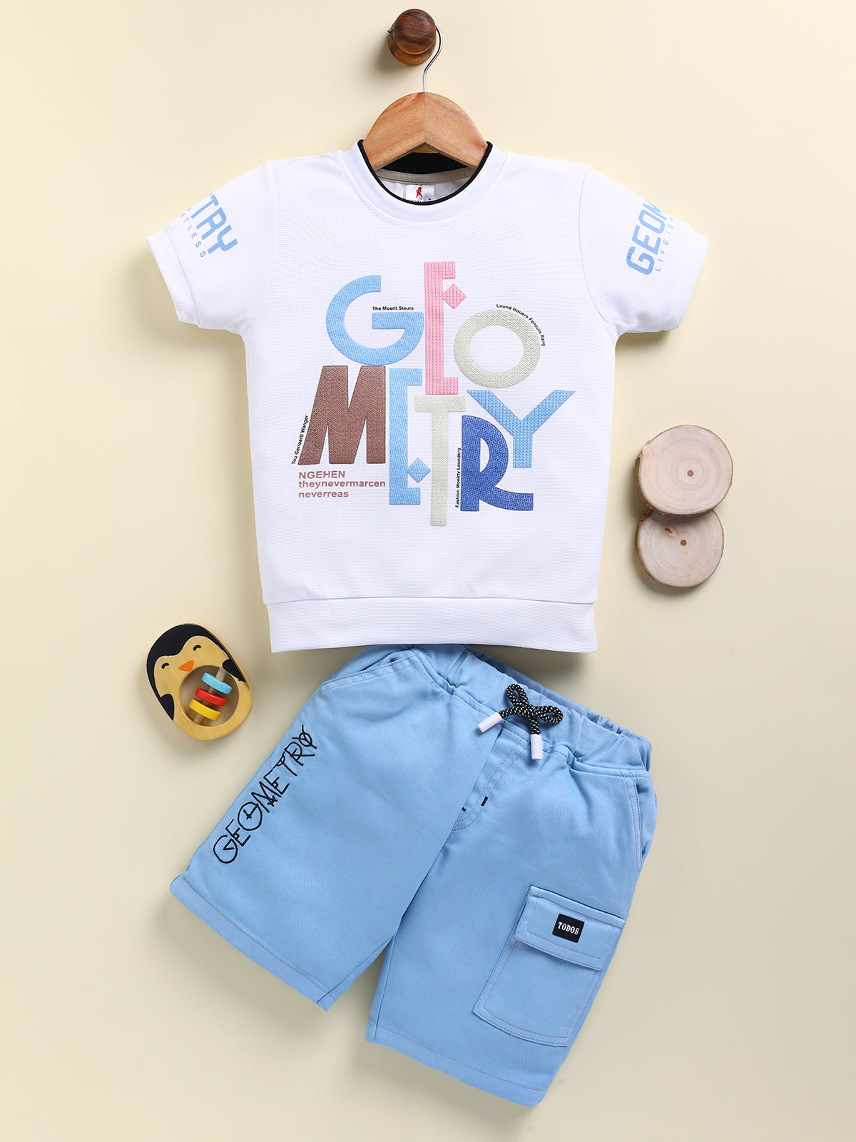 Image file U-19080-Sky Blue.jpg showing a flat lay of a Todos brand boys two-piece clothing set. The outfit includes a white short-sleeve t-shirt with a multi-colored "GEOMETRY" graphic, paired with sky blue cargo shorts featuring a drawstring waist, "GEOMETRY" text on the hem, and a "TODOS" utility patch.