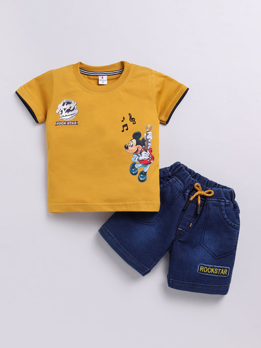 showing a flat lay of a Todos brand boys two-piece clothing set. The outfit features a mustard yellow short-sleeve t-shirt with a graphic of Mickey Mouse playing a guitar and "ROCK STAR" text, paired with dark wash denim shorts featuring an elastic waistband, a mustard yellow drawstring, front pockets, and a "ROCKSTAR" patch on the left leg.