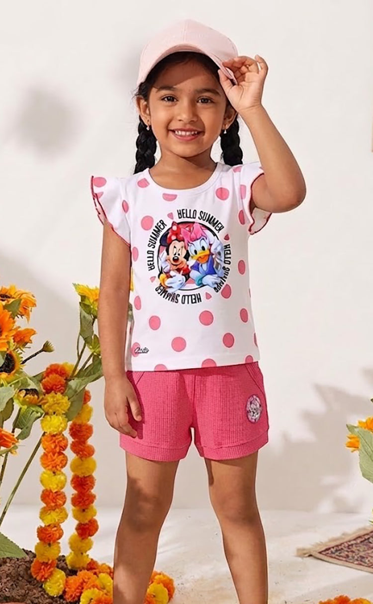 Flat lay of an Annie brand girls two-piece clothing set featuring a white flutter-sleeve top with pink polka dots and a Minnie Mouse and Daisy Duck Hello Summer graphic paired with bright pink textured shorts featuring front pockets belt loops and a small character patch on the left leg.