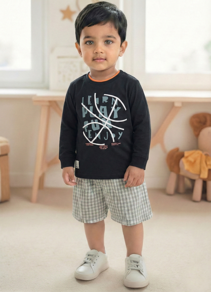 Image file Gemini_Generated_Image_fkez91fkez91fkez.jpg showing a young boy wearing a black Biskid brand boys long-sleeve t-shirt with a basketball-themed "Learn Play Fun Enjoy" graphic on the chest, paired with gray checkered shorts and white sneakers.