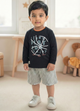 Image file Gemini_Generated_Image_fkez91fkez91fkez.jpg showing a young boy wearing a black Biskid brand boys long-sleeve t-shirt with a basketball-themed "Learn Play Fun Enjoy" graphic on the chest, paired with gray checkered shorts and white sneakers.