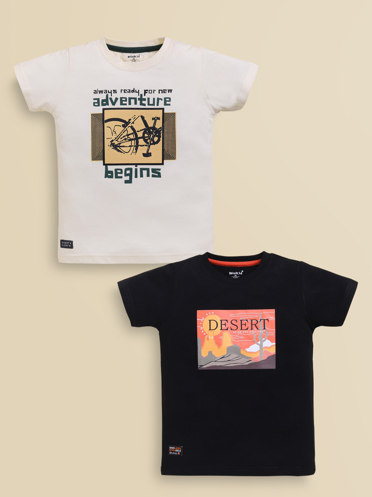 Image file black_creem.jpg showing a 2-pack of Biskid boys short-sleeve t-shirts featuring graphic prints, including an off-white tee with an "adventure begins" bicycle print and a black tee with a "DESERT" sunset landscape graphic.