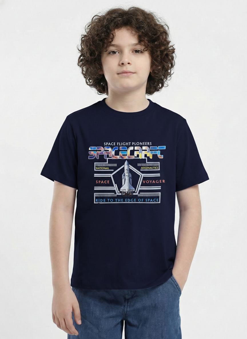 showing a young boy with curly hair modeling a Biskid brand navy blue short-sleeve t-shirt. The shirt features a space-themed chest graphic with a space shuttle, the word "SPACECRAFT" in colorful textured letters, and the text "SPACE FLIGHT PIONEERS" and "RIDE TO THE EDGE OF SPACE".